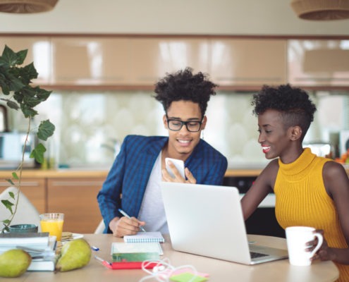 A man and woman smiling as they look over a laptop and mobile device