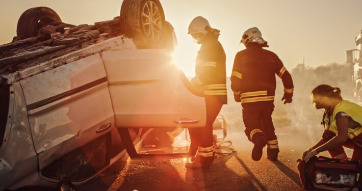 Car Crash Traffic Accident: Paramedics and Firefighters Plan Rescuing Passengers Trapped in Rollover Vehicle. Medics Prepare Stretchers and First Aid Equipment. Firemen Use Hydraulic Cutters Spreader