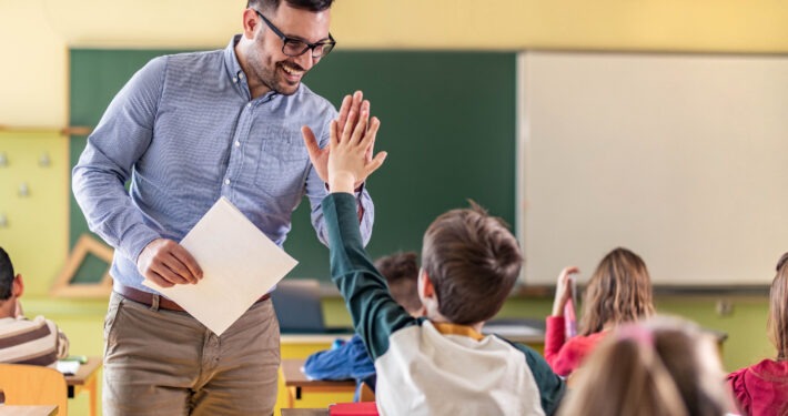 Happy teacher and schoolboy giving each other high-five on a class.